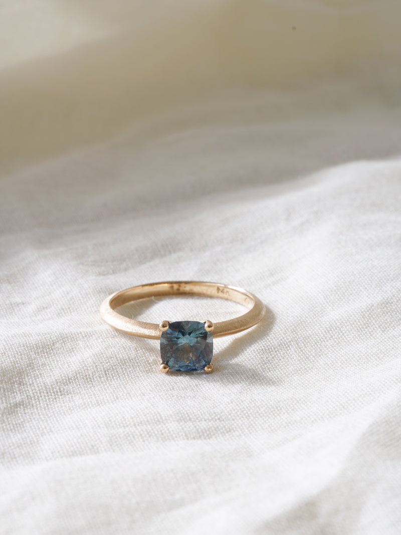 Shown: BIZARRE H - $2090 - Sage Solitaire with a 0.75ct cushion cut teal Montana Sapphire. 14k yellow gold. Organic texture. Matte finish. Size 6