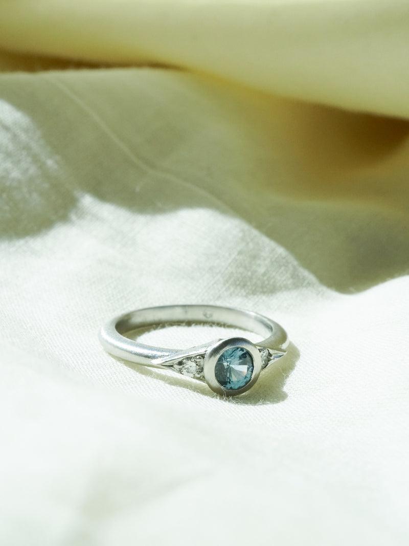 Shown: BIZARRE X - $1445 - Dahlia 3 Stone Ring - 0.25ct Aqua Montana Sapphire with 2mm diamond sides. Platinum. Smooth texture. Matte finish. Size 4.25. 